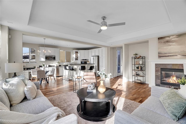 living room featuring a tiled fireplace, light hardwood / wood-style floors, a raised ceiling, and ceiling fan