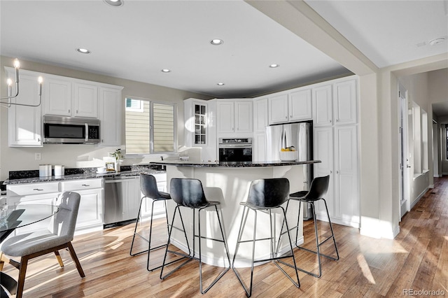 kitchen with appliances with stainless steel finishes, white cabinetry, dark stone counters, a center island, and light wood-type flooring