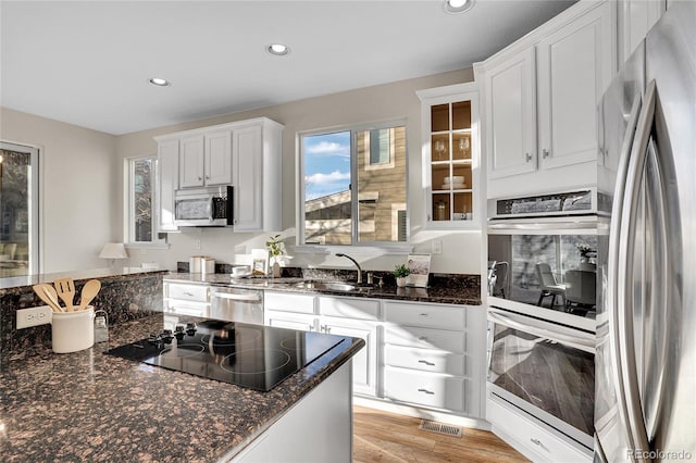 kitchen with appliances with stainless steel finishes, sink, white cabinets, dark stone counters, and light wood-type flooring