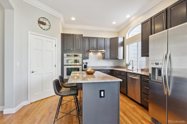 kitchen with light stone countertops, appliances with stainless steel finishes, light hardwood / wood-style flooring, and a kitchen island