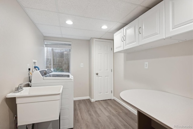 clothes washing area featuring washing machine and dryer, sink, light wood-type flooring, and cabinets