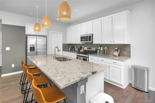 kitchen with sink, hanging light fixtures, appliances with stainless steel finishes, an island with sink, and light stone countertops