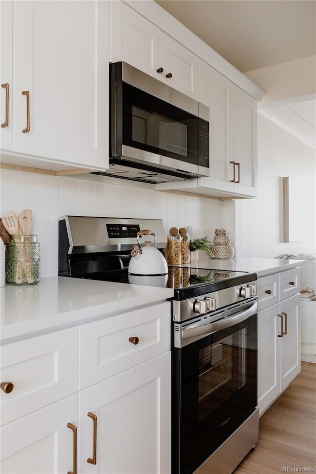 kitchen featuring white cabinets, tasteful backsplash, appliances with stainless steel finishes, and light hardwood / wood-style flooring