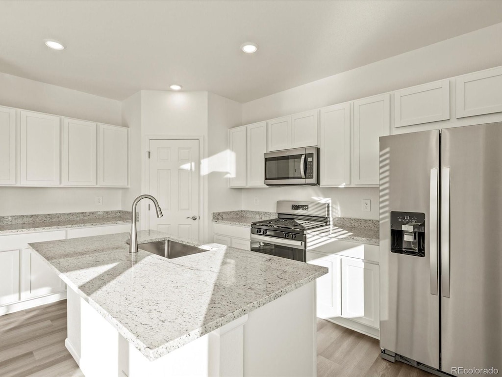 kitchen with sink, appliances with stainless steel finishes, a kitchen island with sink, white cabinetry, and light stone countertops