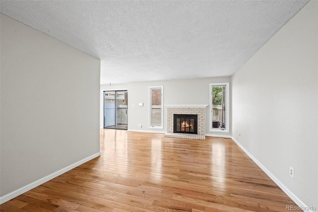 unfurnished living room with light wood-type flooring, a textured ceiling, a brick fireplace, and baseboards