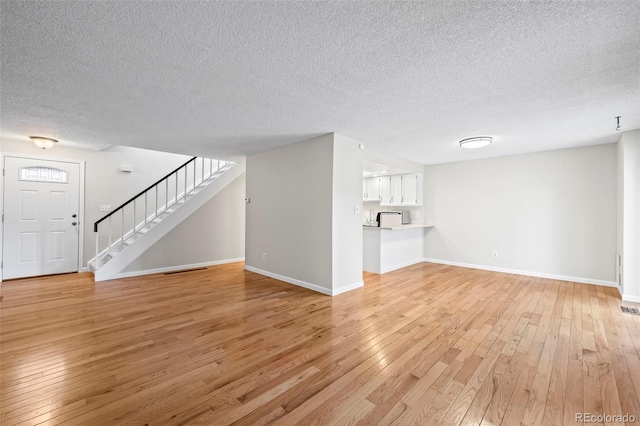 unfurnished living room with light wood-type flooring, a textured ceiling, stairs, and baseboards
