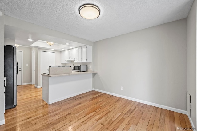 kitchen with stainless steel appliances, light wood finished floors, a peninsula, baseboards, and a textured ceiling