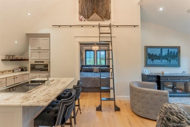 kitchen with a kitchen breakfast bar, oven, vaulted ceiling, light stone countertops, and light wood-type flooring