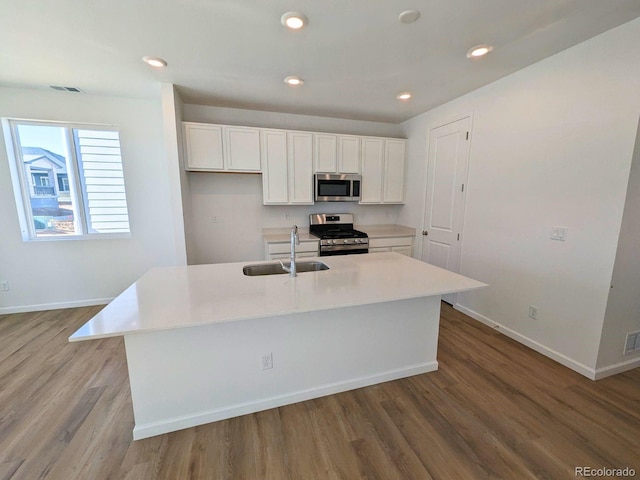 kitchen with wood finished floors, a sink, white cabinetry, baseboards, and appliances with stainless steel finishes