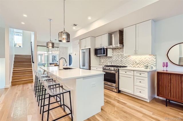 kitchen with high end appliances, wall chimney range hood, a sink, tasteful backsplash, and a kitchen island with sink