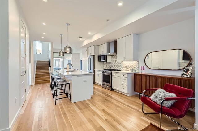 kitchen with high quality appliances, a sink, light wood-style flooring, white cabinets, and backsplash