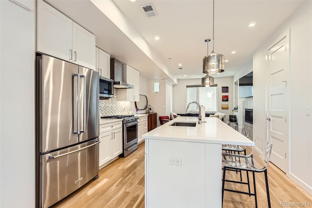 kitchen with premium appliances, a sink, wall chimney exhaust hood, light wood-type flooring, and light countertops