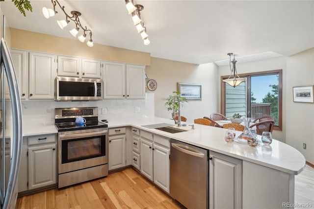 kitchen with backsplash, light countertops, a peninsula, stainless steel appliances, and light wood-style flooring