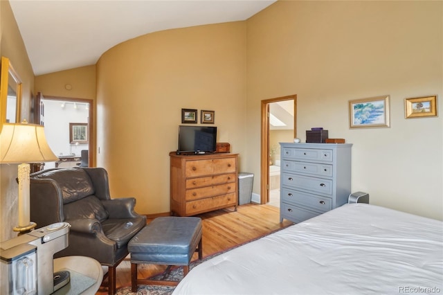 bedroom featuring vaulted ceiling, ensuite bath, and light wood-style flooring