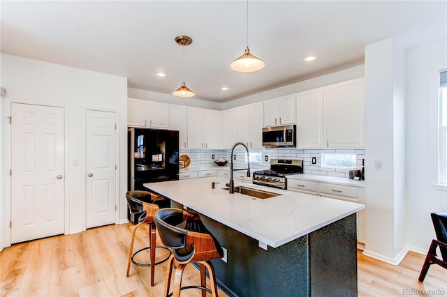 kitchen with appliances with stainless steel finishes, tasteful backsplash, a sink, light wood finished floors, and white cabinetry