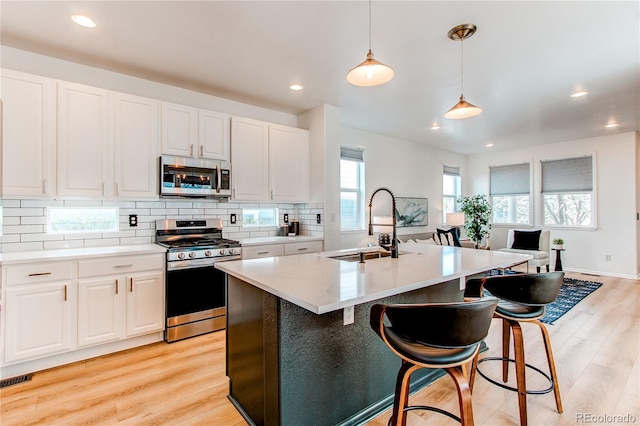 kitchen with appliances with stainless steel finishes, a sink, light wood-style floors, decorative light fixtures, and tasteful backsplash