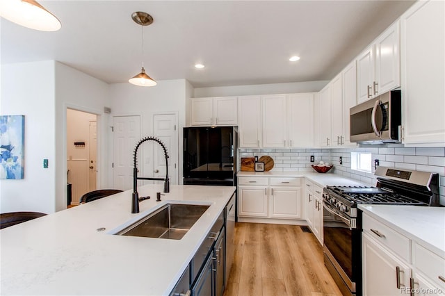 kitchen featuring white cabinets, appliances with stainless steel finishes, a sink, and light wood-type flooring