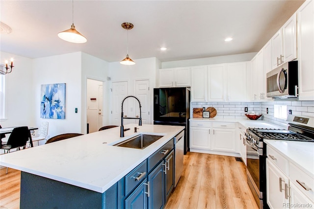 kitchen featuring white cabinets, a sink, light wood finished floors, blue cabinetry, and stainless steel appliances