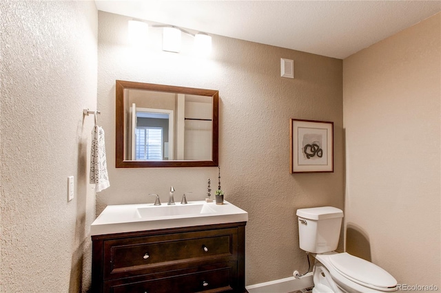 half bath with a textured wall, vanity, toilet, baseboards, and visible vents