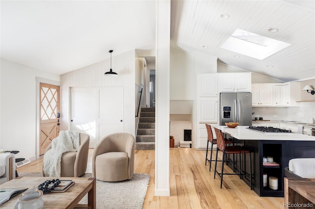 kitchen with stainless steel refrigerator with ice dispenser, light wood finished floors, white cabinetry, gas cooktop, and a kitchen breakfast bar