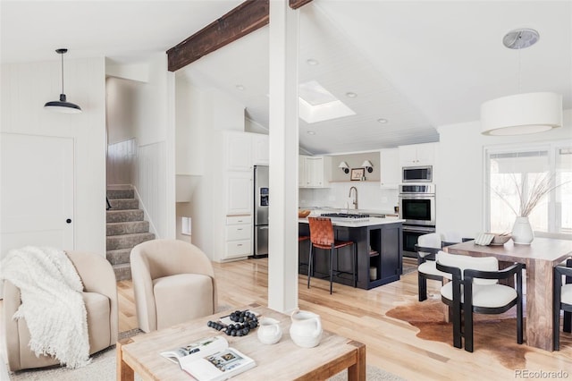 living area with vaulted ceiling with skylight, stairway, and light wood-type flooring