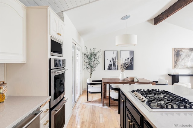 kitchen featuring vaulted ceiling with beams, light wood finished floors, appliances with stainless steel finishes, and light countertops