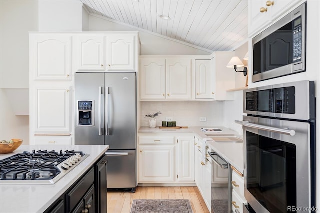 kitchen featuring stainless steel appliances, white cabinetry, vaulted ceiling, light countertops, and backsplash