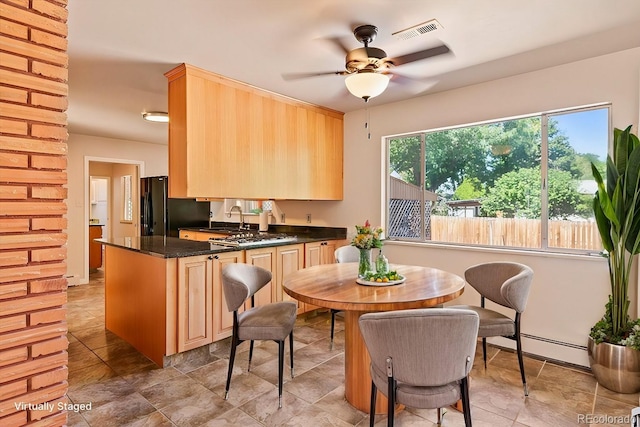 kitchen with light brown cabinets, freestanding refrigerator, a ceiling fan, visible vents, and a baseboard radiator