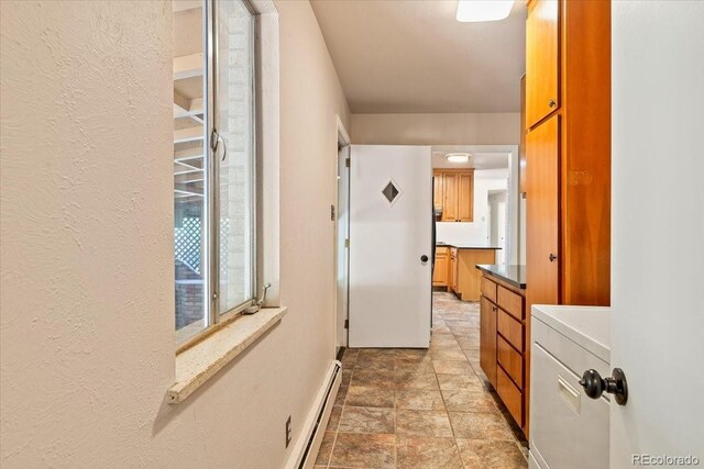 hallway with baseboards, a textured wall, stone finish floor, washer / dryer, and a baseboard radiator