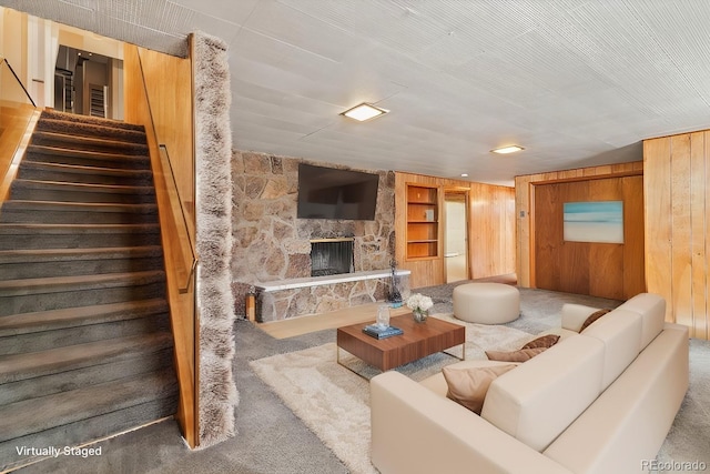 living area with built in features, a fireplace, stairway, carpet floors, and wood walls