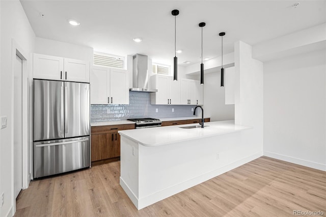 kitchen with wall chimney exhaust hood, sink, white cabinetry, hanging light fixtures, and stainless steel appliances