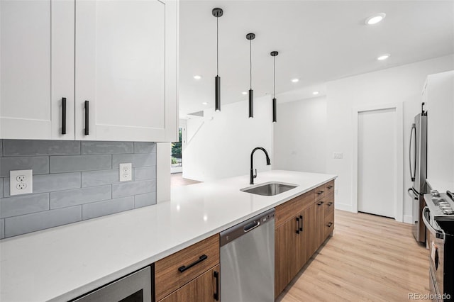 kitchen with pendant lighting, tasteful backsplash, sink, white cabinets, and stainless steel appliances