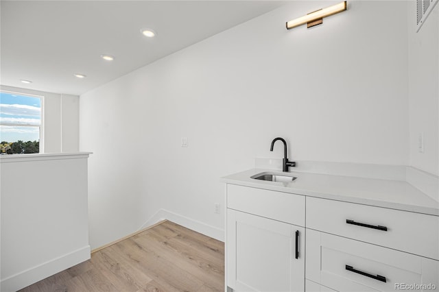 bar featuring sink, white cabinets, and light hardwood / wood-style floors