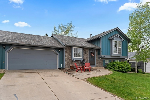 tri-level home with board and batten siding, a front yard, a garage, concrete driveway, and stone siding