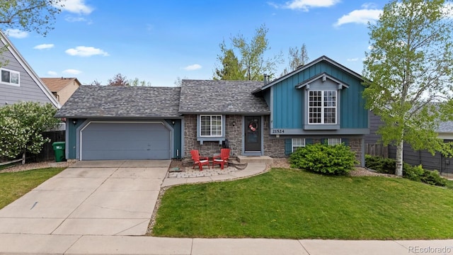 tri-level home featuring an attached garage, stone siding, concrete driveway, a front lawn, and board and batten siding