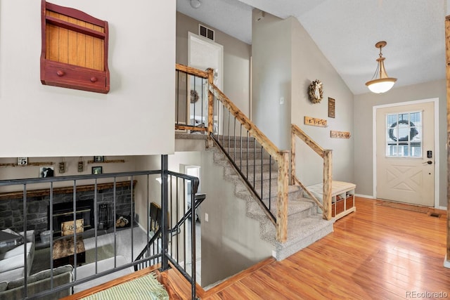foyer featuring light wood-type flooring, visible vents, baseboards, lofted ceiling, and stairs