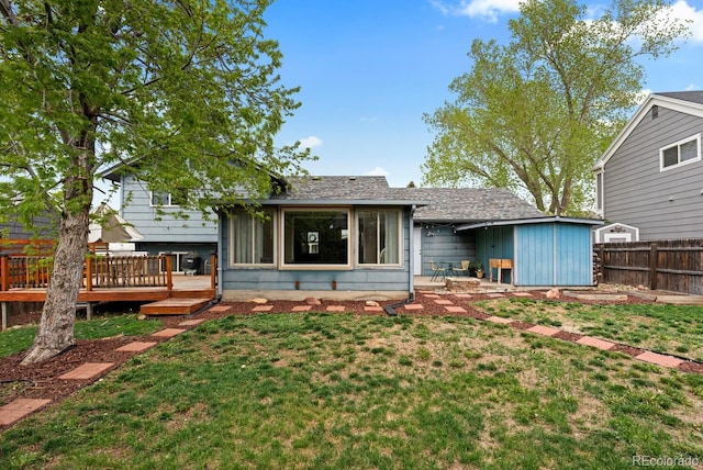 rear view of house with a lawn, a wooden deck, roof with shingles, and fence