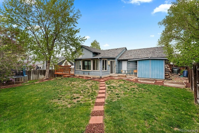 ranch-style home featuring a trampoline, a wooden deck, a front yard, and a fenced backyard