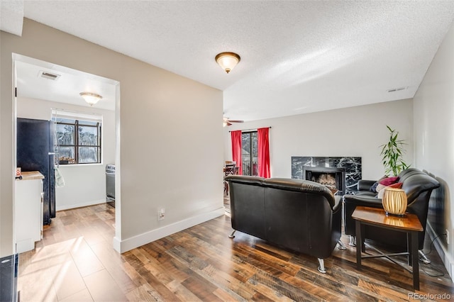 living room with dark hardwood / wood-style flooring, a textured ceiling, a high end fireplace, and a healthy amount of sunlight