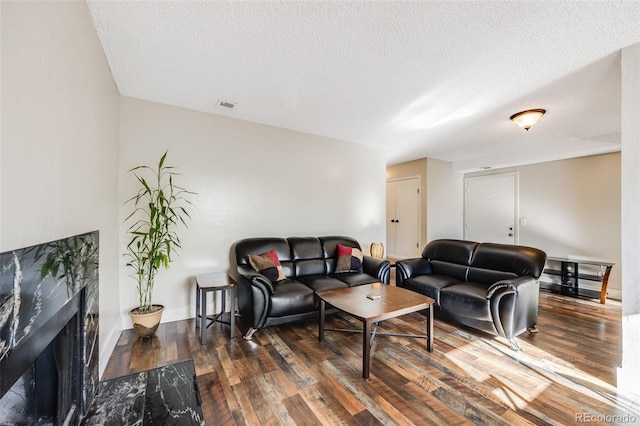 living room featuring a premium fireplace, dark wood-type flooring, and a textured ceiling