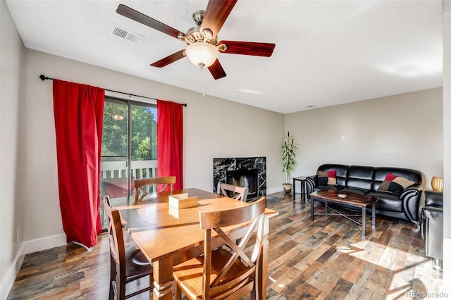 dining room featuring ceiling fan, a high end fireplace, dark hardwood / wood-style flooring, and a textured ceiling