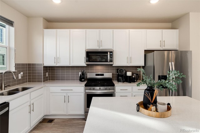 kitchen with tasteful backsplash, white cabinets, stainless steel appliances, and a sink