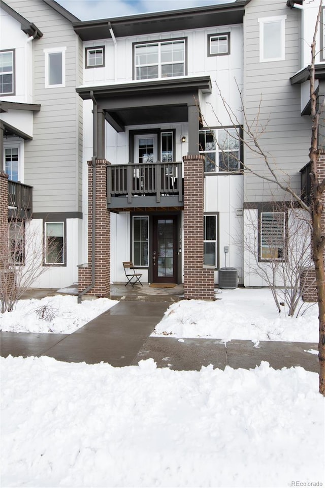 snow covered rear of property with board and batten siding and central AC