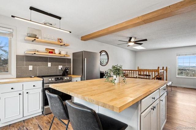 kitchen with a kitchen bar, white cabinetry, wooden counters, appliances with stainless steel finishes, and a kitchen island