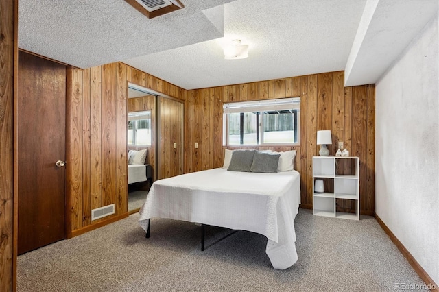 bedroom featuring carpet flooring, wood walls, a textured ceiling, and a closet