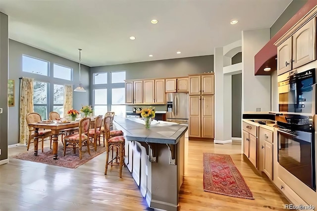 kitchen featuring stainless steel appliances, a towering ceiling, light hardwood / wood-style flooring, light brown cabinetry, and decorative light fixtures