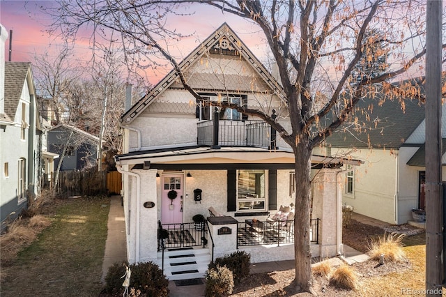 victorian house with a porch, fence, a balcony, and stucco siding