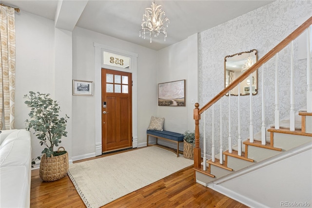 entryway with wood finished floors, baseboards, stairs, wallpapered walls, and an inviting chandelier