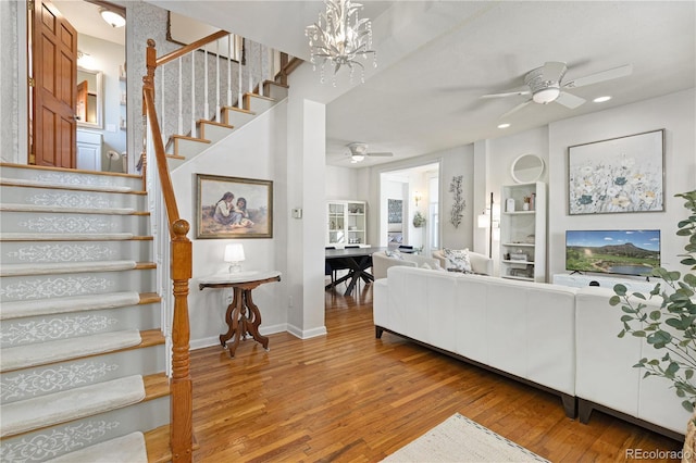 living area featuring baseboards, stairway, wood finished floors, and ceiling fan with notable chandelier