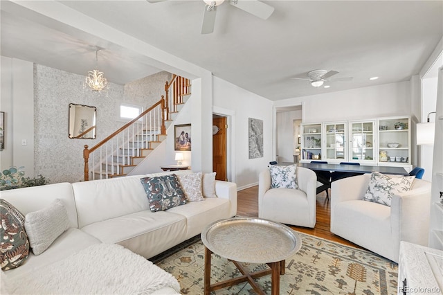 living room with stairway, a ceiling fan, an accent wall, wood finished floors, and baseboards